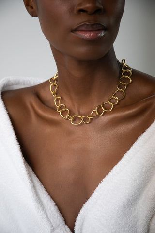 Close-up of medium-dark woman's neck and chest wearing a thick gold chain with irregular rounded links over a white V-neck.