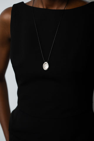 Close-up, eye-level view of a silver embossed pendant on a thin black cord worn over a sleeveless black dress.
