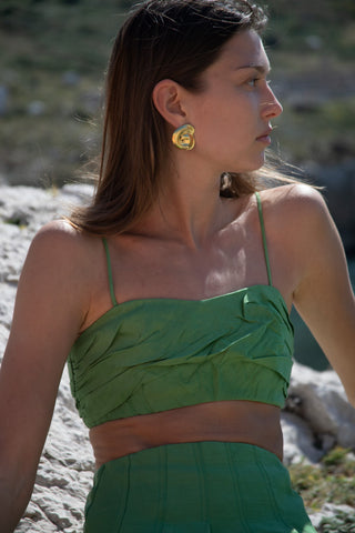 Side-profile of woman in a green crop top seated on a rock, wearing a large gold abstract hoop earring on her left ear