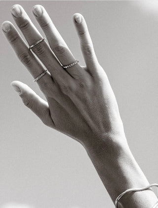 Close-up black-and-white left hand wearing four simple rings with smooth and twisted textures and a metal bangle.