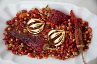 White dish of small dried red chillies with three larger ones, two gold‑toned metallic open‑geometric spheres nestled on top