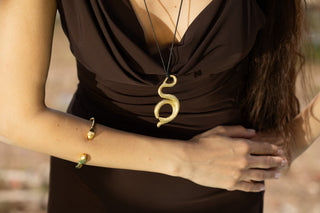 Torso in fitted brown sleeveless dress wearing gold snake bracelet and matching gold snake necklace on black string
