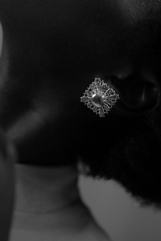 Monochrome close-up of a dark-skinned profile wearing an ornate square earring with a central spherical detail.