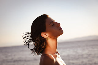 Close-up profile of a woman at golden hour wearing a large round gold sun-shaped earring