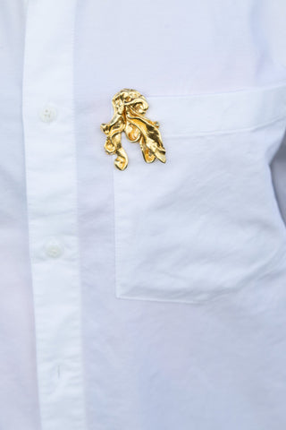 Close-up of white button-up shirt pocket with an abstract gold metallic decorative pin attached.
