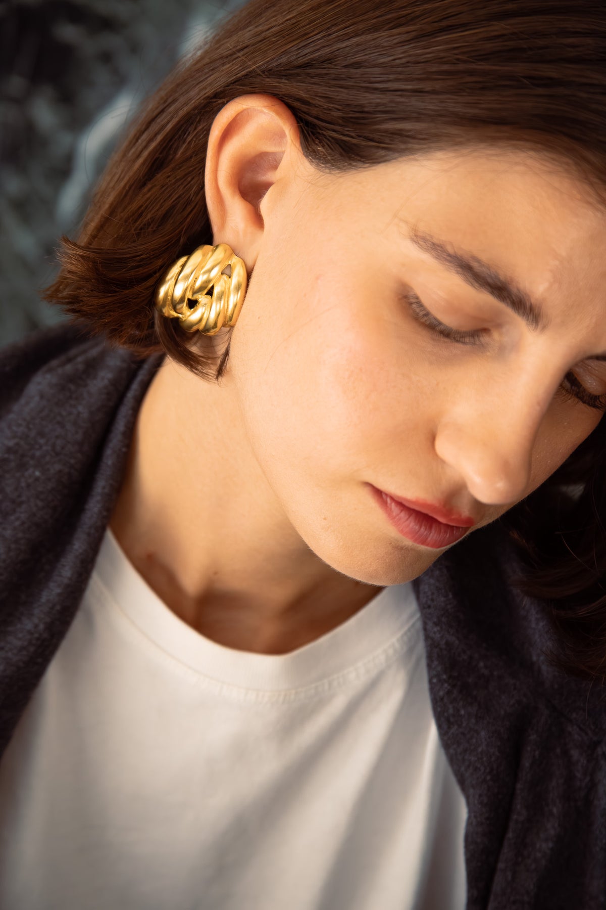 Close-up profile of a young woman wearing a large shiny gold-coloured statement earring.