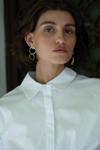 Person wearing a white shirt with gold chain hoop earrings against a blurred background